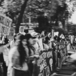 Segmento di manifestazione femminista, persone tengono in mano uno striscione, foto in bianco e nero con effetto mosso che rende poco chiari i volti