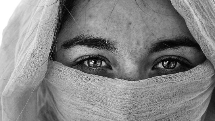 Il volto di una ragazza in bianco nero, coperto in parte da un velo. Si vedono solo gli occhi, chiari e intensi