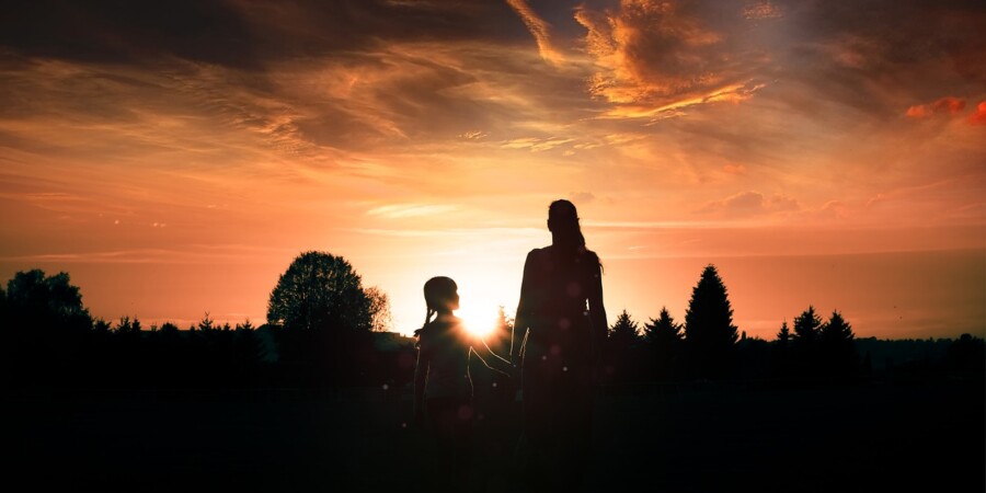 Due sagome in controluce, una donna e una bambina, guardano insieme il tramonto