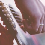Una mano femminile con un anello al dito suona le corde di una chitarra