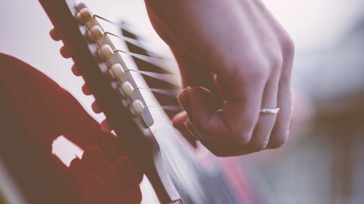 Una mano femminile con un anello al dito suona le corde di una chitarra